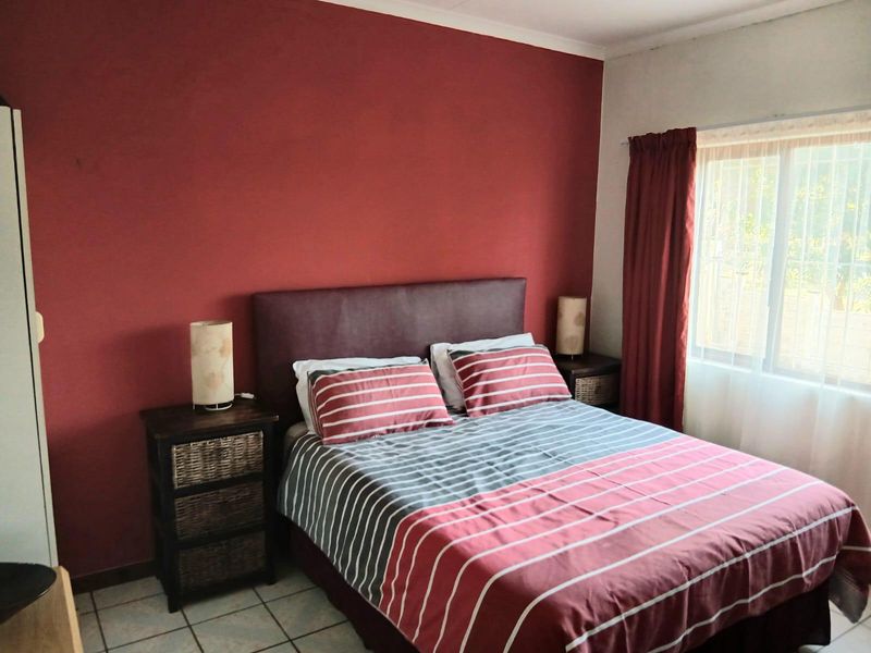 A bedroom featuring tiled flooring and a window with security bars, finished with a bold red accent wall.