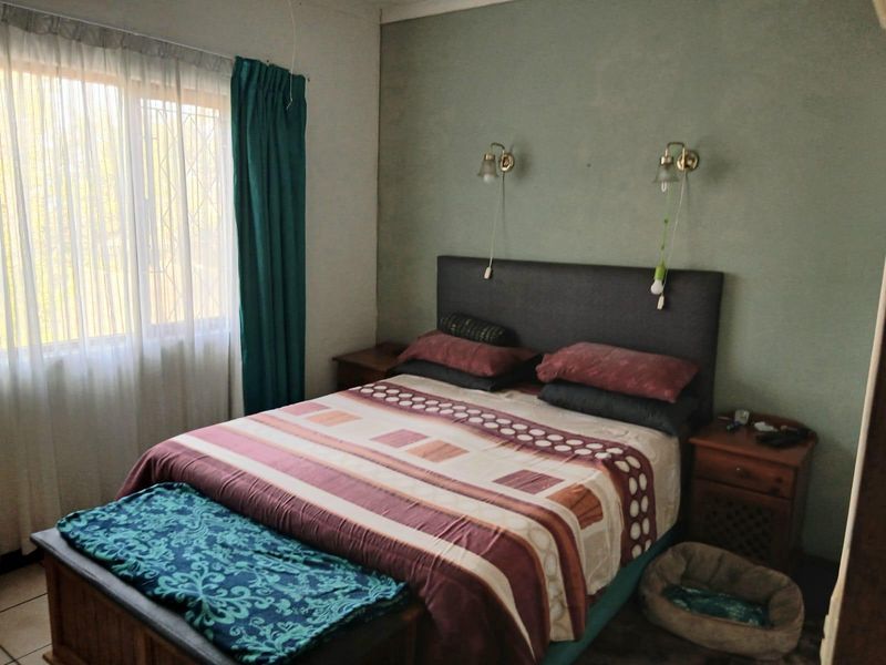 A standard bedroom featuring a large window with security bars and wall-mounted light fixtures above the bed area.