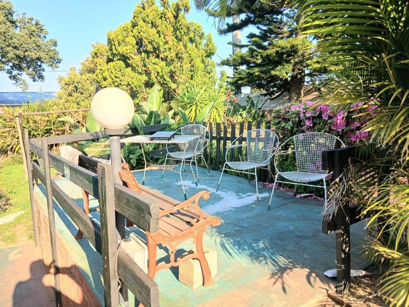 An outdoor patio area featuring a concrete surface and timber fencing, surrounded by established garden greenery.