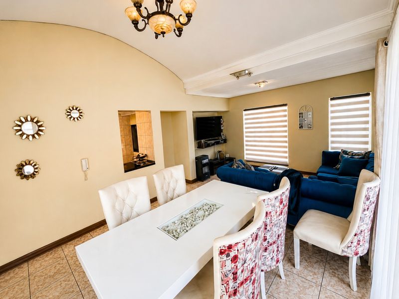 Open-plan living and dining area featuring tiled floors, a vaulted ceiling with decorative molding, and a convenient pass-through window to the kitchen.