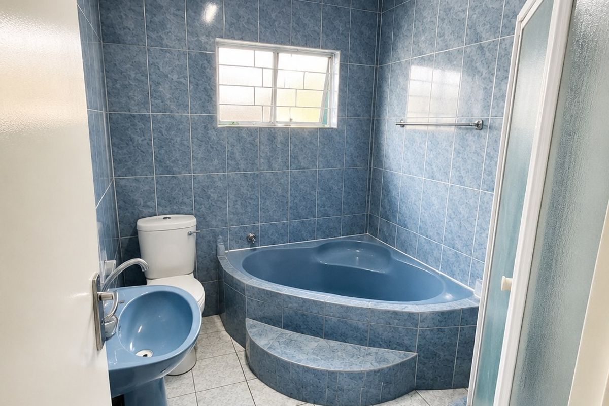 A dated bathroom featuring blue tiled walls, a corner bathtub, a pedestal basin, a toilet, and a separate shower enclosure.