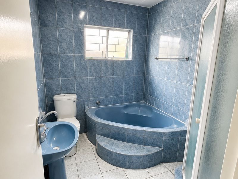 A dated bathroom featuring blue tiled walls, a corner bathtub, a pedestal basin, a toilet, and a separate shower enclosure.