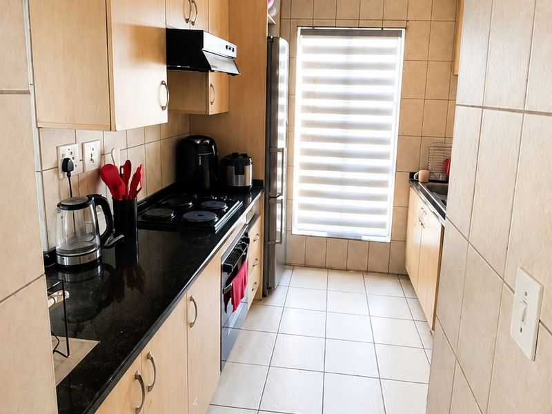 A functional galley-style kitchen featuring light wood cabinetry, dark granite countertops, tiled finishes, and integrated cooking appliances.