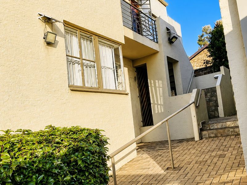 Rear exterior view of the townhouse featuring a paved walkway, metal handrail, and an upper-level balcony with metal balustrade.