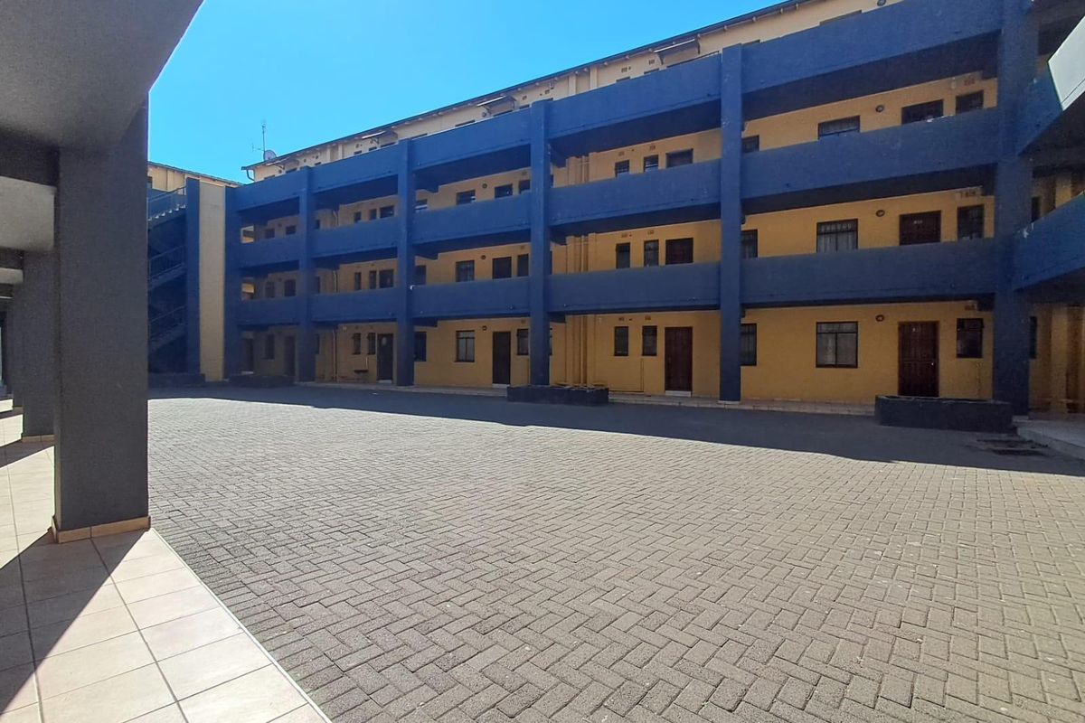 A view of the paved courtyard and rear facade of a multi-story apartment complex featuring external walkways and stairwell access.