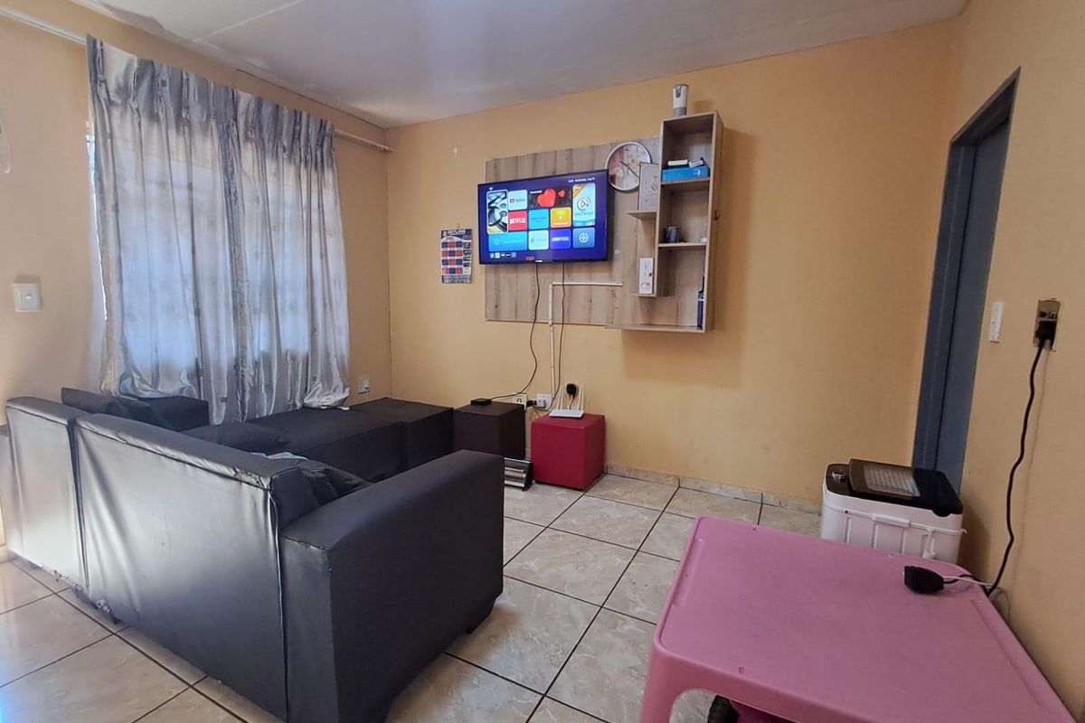 A living room featuring tiled flooring and a wall-mounted shelving unit, providing a functional space that could benefit from cosmetic updates.
