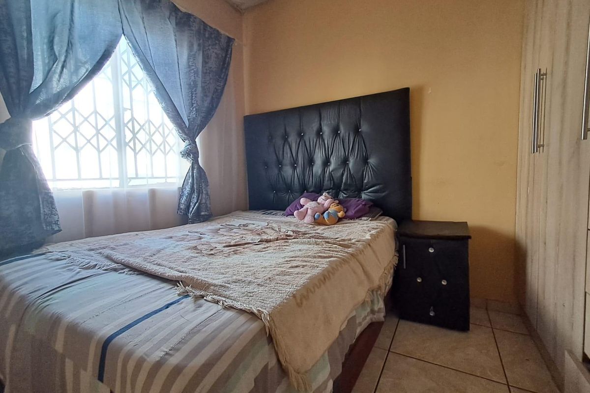 A bedroom featuring tiled flooring, a built-in wardrobe, and a security gate on the window. The ceiling shows signs of water damage.