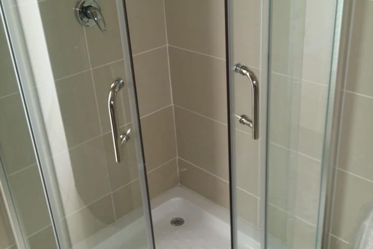 A clean, modern corner shower enclosure with glass doors, chrome fixtures, and neutral wall tiling in a well-maintained bathroom.