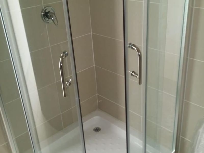 A clean, modern corner shower enclosure with glass doors, chrome fixtures, and neutral wall tiling in a well-maintained bathroom.