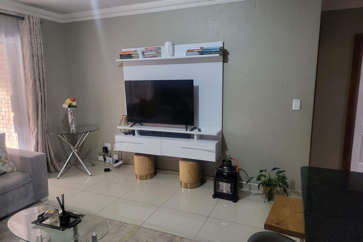 A living room featuring a modern white wall-mounted media console, neutral wall paint, and polished floor tiles.