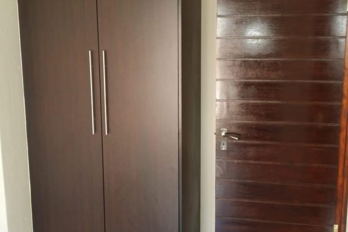 A clean bedroom interior featuring a dark wood built-in wardrobe, matching internal door, and neutral tiled flooring.