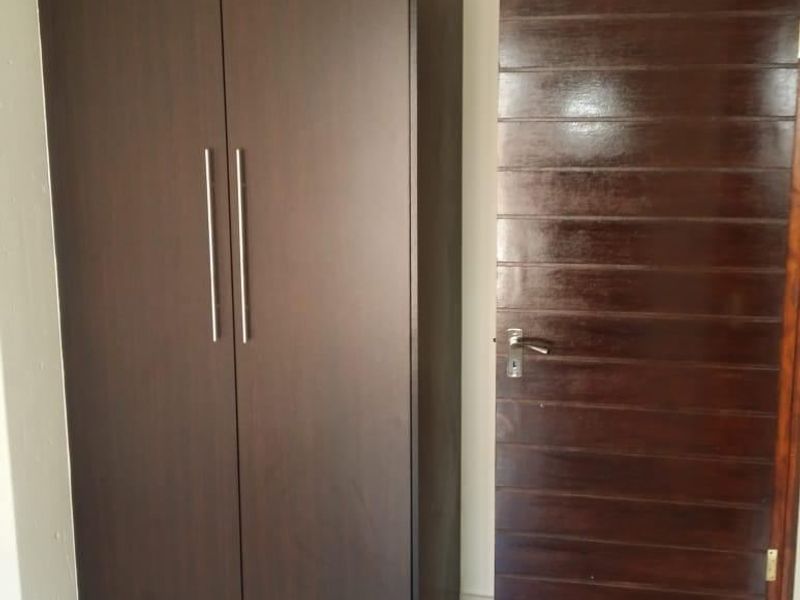 A clean bedroom interior featuring a dark wood built-in wardrobe, matching internal door, and neutral tiled flooring.