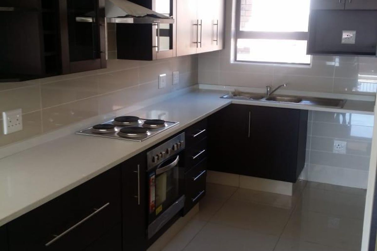 Modern kitchen featuring dark wood cabinetry, stone countertops, built-in oven, electric hob, and tiled finishes throughout.