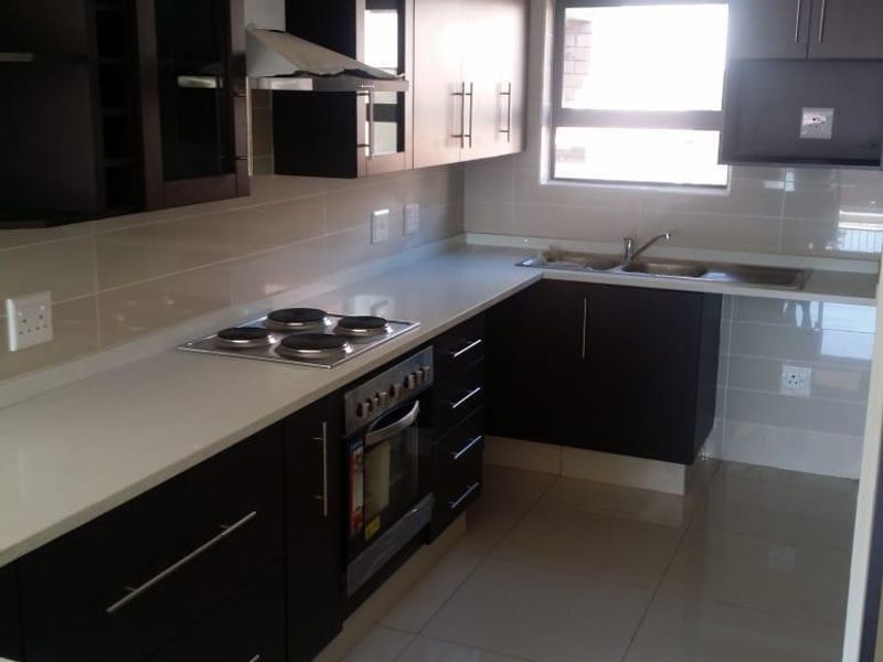 Modern kitchen featuring dark wood cabinetry, stone countertops, built-in oven, electric hob, and tiled finishes throughout.