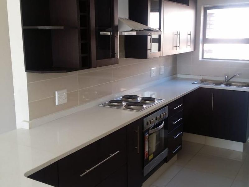 Modern kitchen featuring dark wood cabinetry, stone countertops, built-in oven, electric hob, and a double bowl sink with tiled finishes.