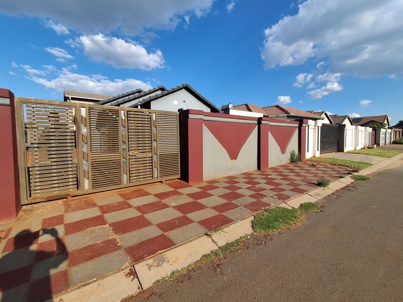 Front exterior view of the property featuring a secure sliding gate, perimeter wall, and a checkered paved driveway.