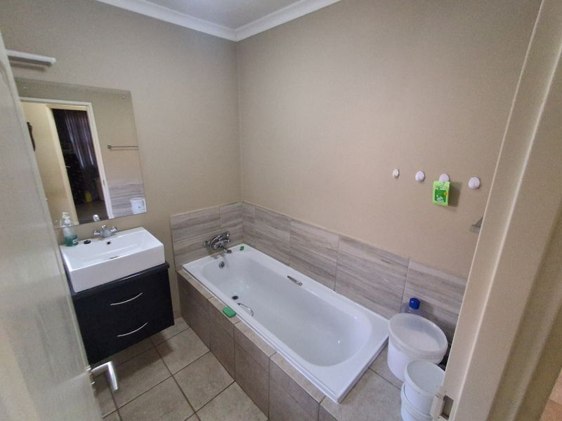 A functional bathroom featuring a built-in bathtub with tiled surround, a modern vanity cabinet with basin, and neutral wall finishes.