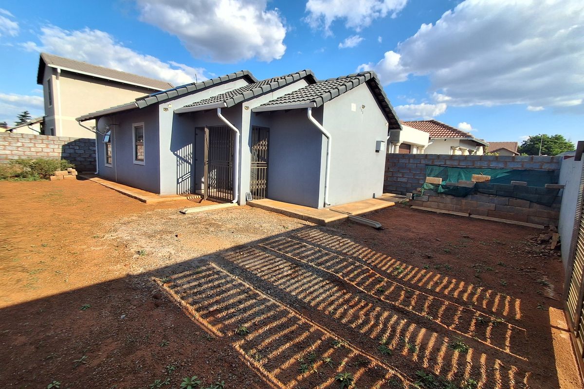 Rear view of the property featuring a tiled roof, security gates, and an expansive, undeveloped garden area with boundary walls.