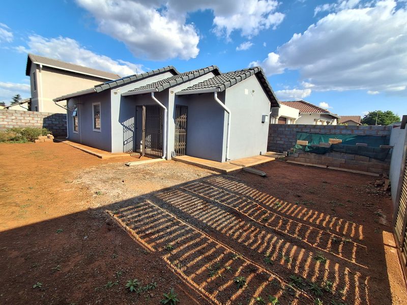 Rear view of the property featuring a tiled roof, security gates, and an expansive, undeveloped garden area with boundary walls.