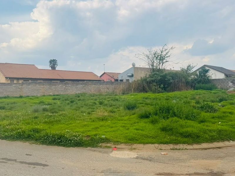 A vacant residential plot featuring a grassed surface, boundary wall, and street access, situated in a developed neighborhood.