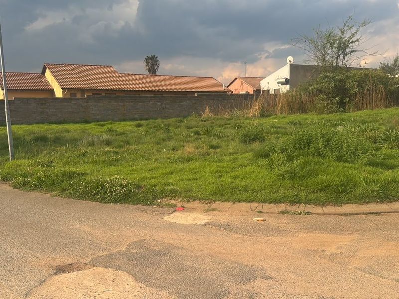 A vacant residential plot situated in a developed neighborhood, featuring street access and perimeter walling, ready for new construction.
