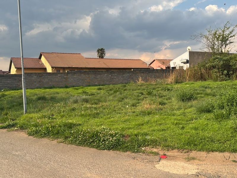 A vacant residential plot featuring grass coverage and a perimeter boundary wall, situated in a developed neighborhood.