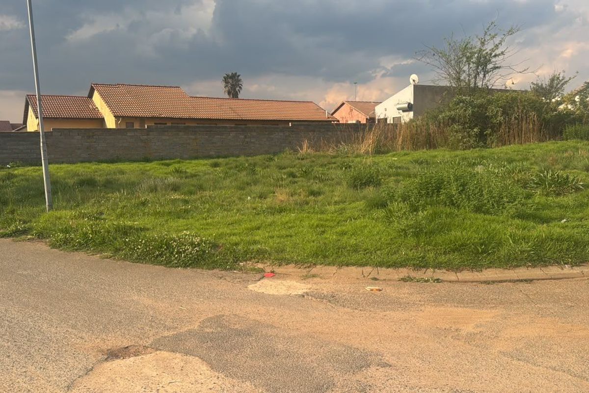 A vacant residential plot featuring a perimeter wall and direct street access, situated in a developed neighborhood.