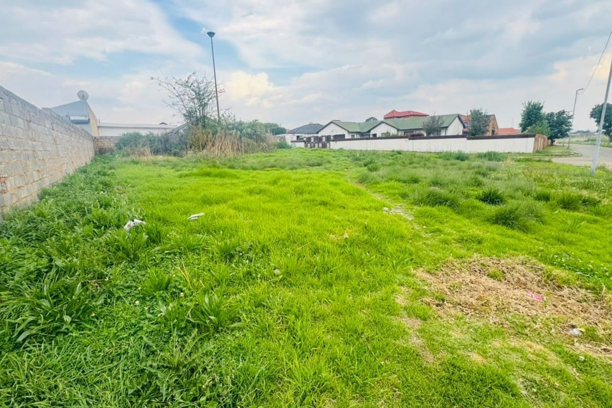 A vacant residential plot featuring a perimeter wall and street access, suitable for new development.
