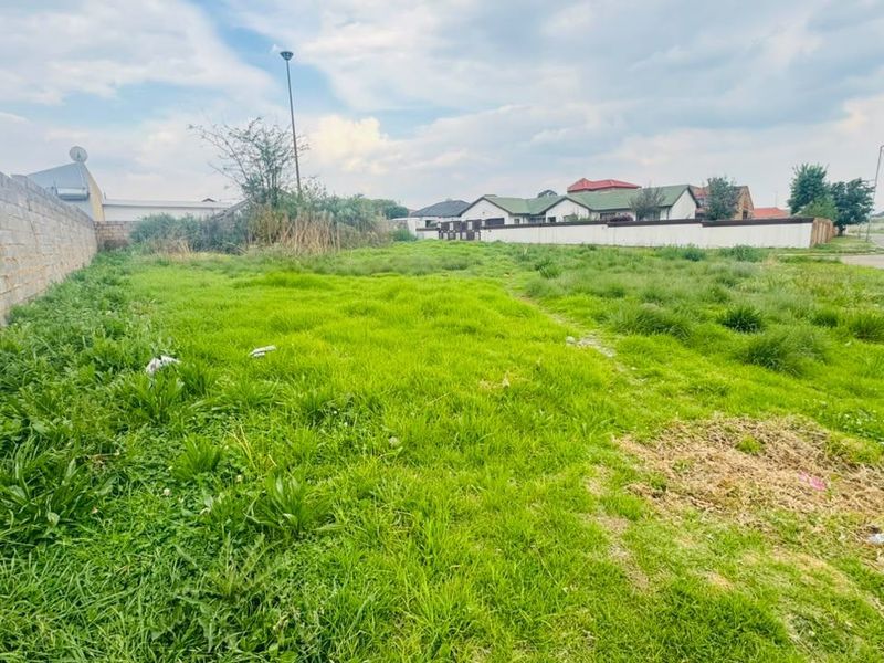 A vacant residential plot featuring a perimeter wall and street access, suitable for new development.