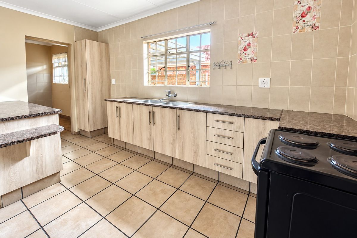 A functional kitchen featuring light wood-look cabinetry, granite-style laminate countertops, tiled flooring, and a double basin sink with a window view.