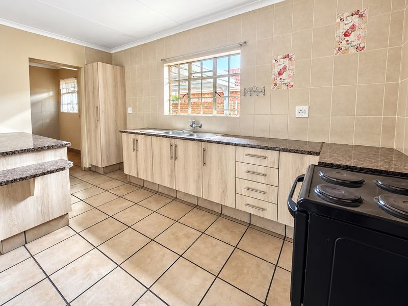 A functional kitchen featuring light wood-look cabinetry, granite-style laminate countertops, tiled flooring, and a double basin sink with a window view.