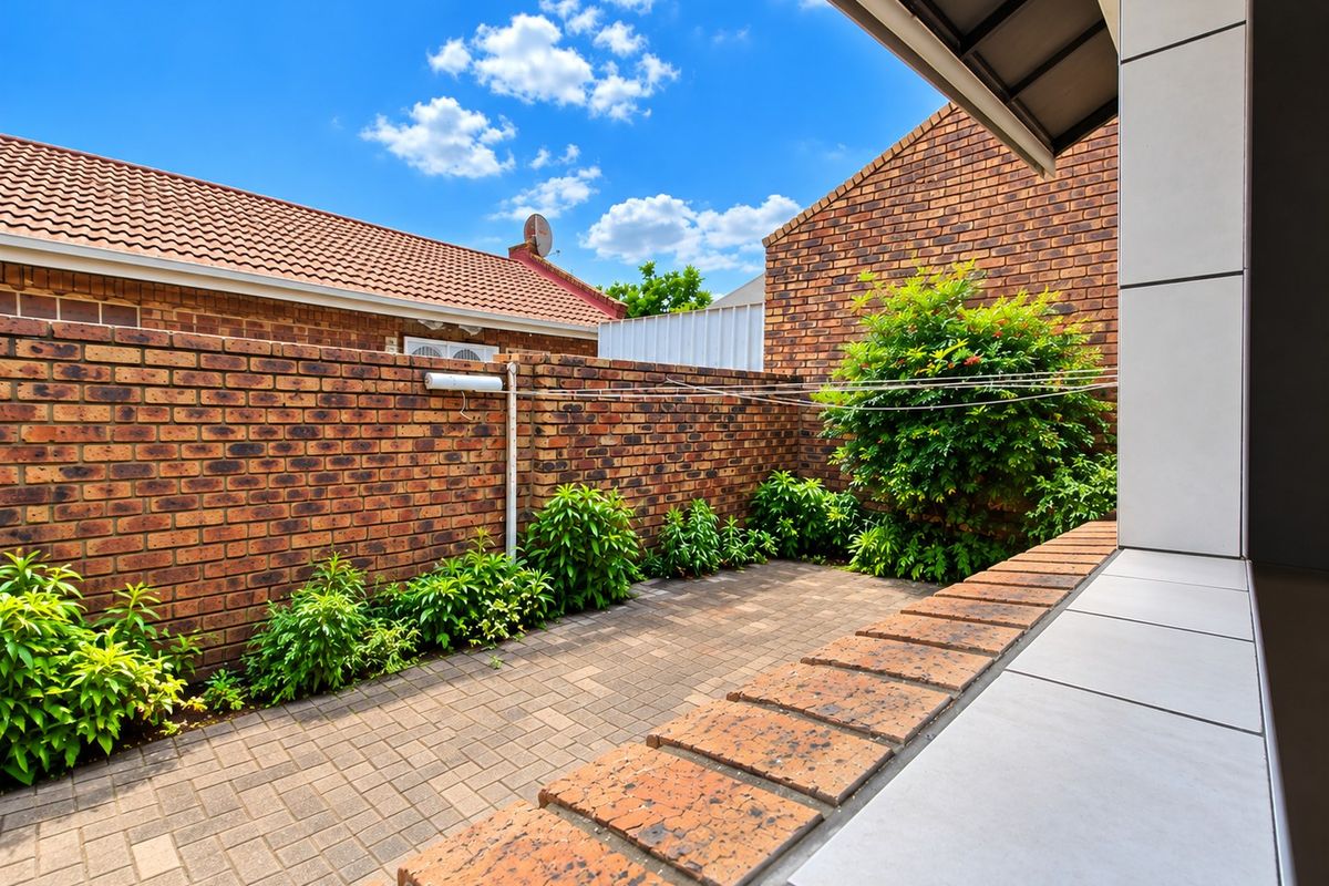 A private rear courtyard featuring a paved patio area, brick boundary walls, and established garden greenery.