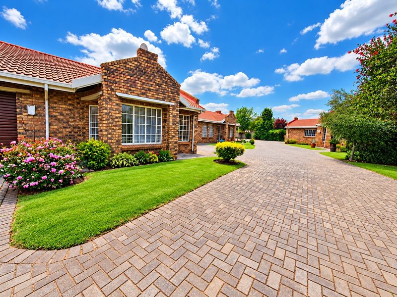 Well-maintained face brick residential property featuring a spacious paved driveway, manicured lawn, and classic terracotta roof tiles.