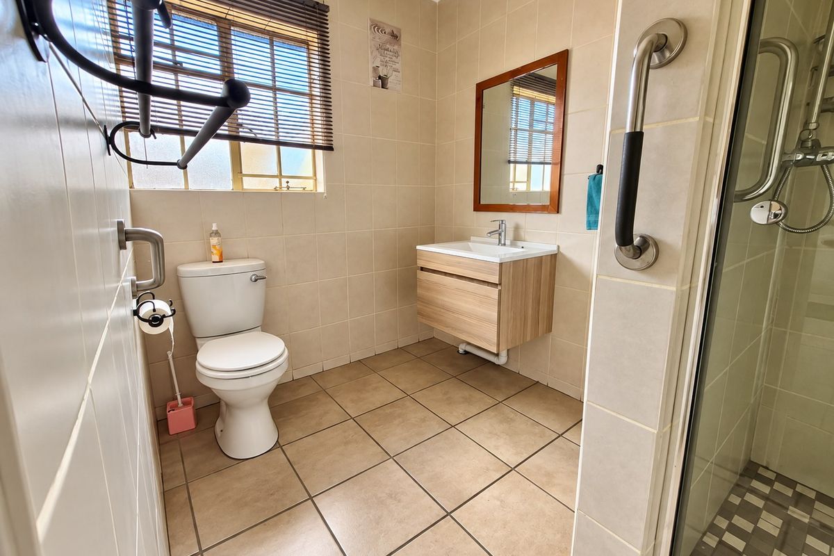 A functional bathroom featuring a wall-mounted vanity, tiled walls and flooring, a shower enclosure, and safety grab rails.
