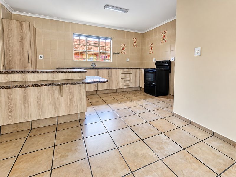 A clean, functional kitchen featuring light wood-look cabinetry, granite countertops, tiled flooring, and a freestanding stove, offering a neutral canvas for updates.