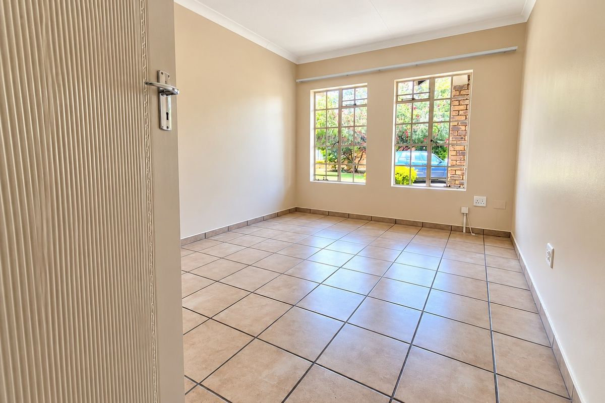 A bright, empty bedroom featuring neutral tiled flooring, coved ceilings, and large steel-framed windows allowing for natural light.