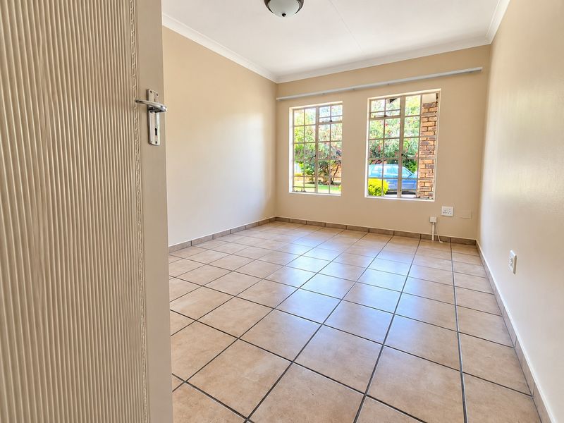 A bright, empty bedroom featuring neutral tiled flooring, coved ceilings, and large steel-framed windows allowing for natural light.