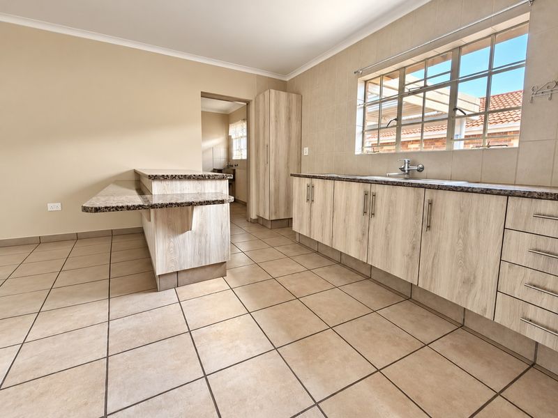 A clean, modern kitchen featuring light wood-look cabinetry, granite countertops, a breakfast bar, and neutral tiled flooring, offering a functional and well-maintained space.