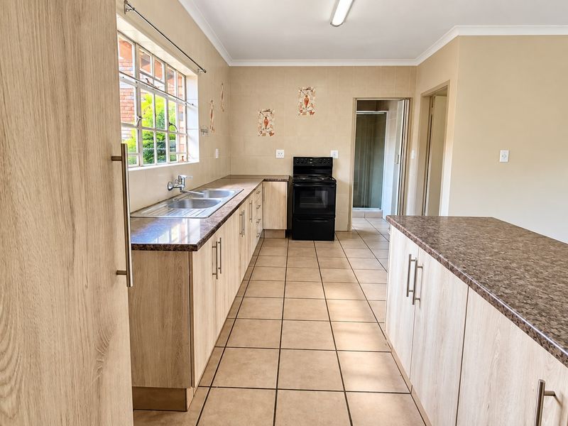 A functional kitchen featuring light wood-look cabinetry, laminate countertops, a stainless steel double sink, and a freestanding electric stove with tiled flooring.