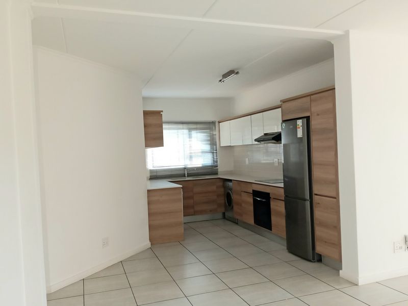 Modern kitchen featuring wood-finish cabinetry, white gloss upper cabinets, tiled flooring, and integrated appliances including an oven, hob, and extractor fan.