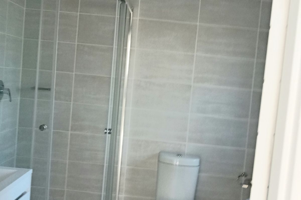 A modern bathroom featuring a glass shower enclosure, a white toilet, and a vanity cabinet with neutral wall and floor tiling.