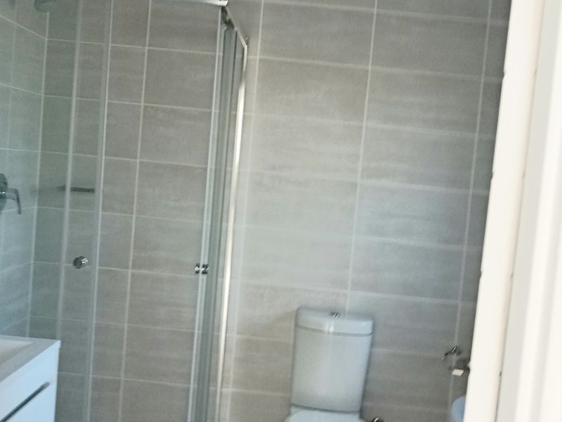 A modern bathroom featuring a glass shower enclosure, a white toilet, and a vanity cabinet with neutral wall and floor tiling.