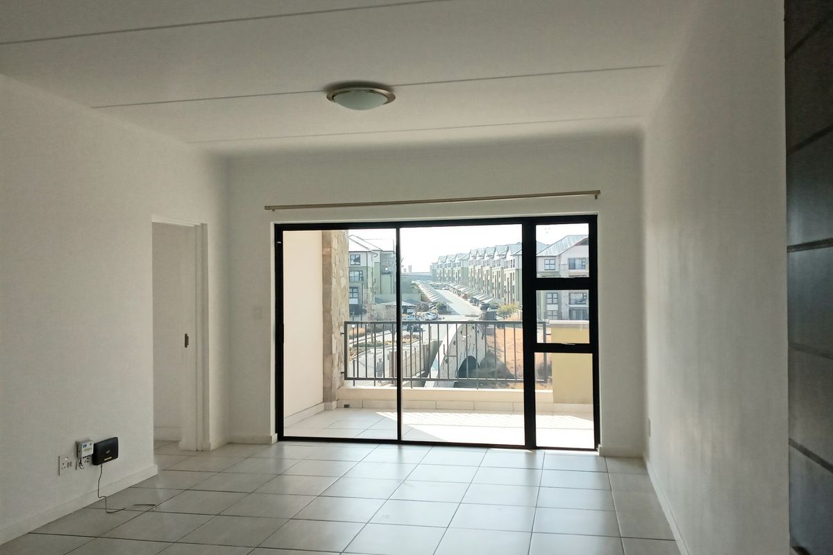 An empty, well-lit living area featuring neutral tiled flooring and a large sliding glass door providing access to a private balcony.