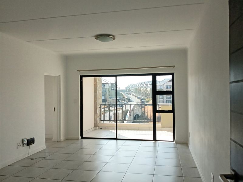 An empty, well-lit living area featuring neutral tiled flooring and a large sliding glass door providing access to a private balcony.