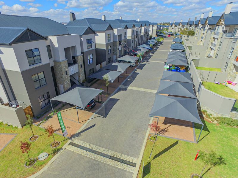 Aerial view of a modern apartment complex featuring paved driveways, designated shade cloth carports, and well-maintained landscaped grounds.