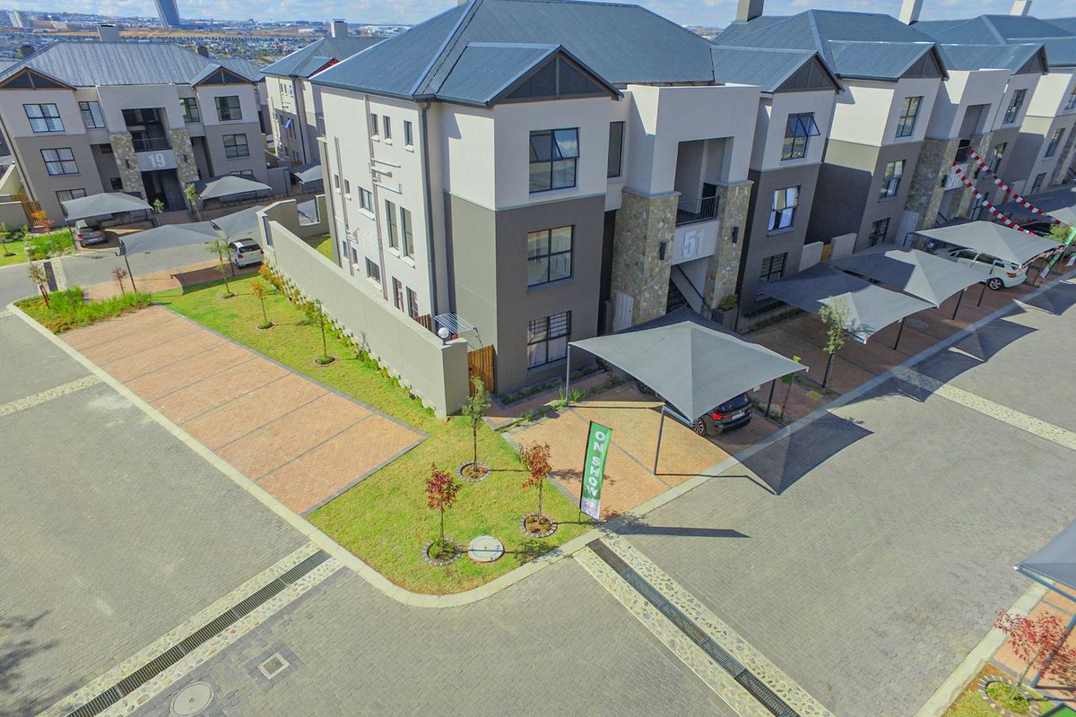 Aerial view of a modern apartment complex featuring paved driveways, covered parking bays, and well-maintained communal garden areas.