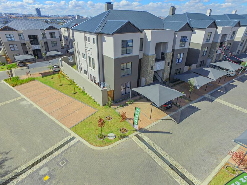 Aerial view of a modern apartment complex featuring paved driveways, covered parking bays, and well-maintained communal garden areas.