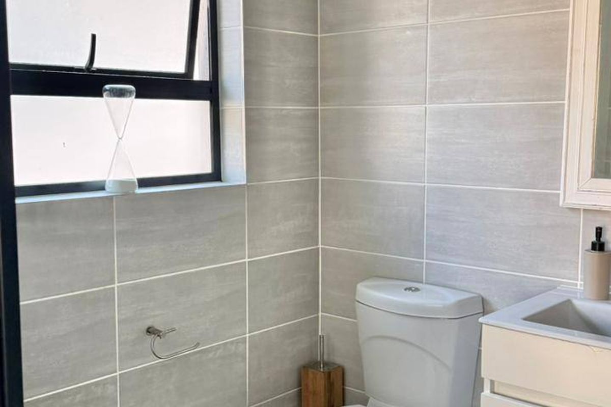 A modern, well-maintained bathroom featuring neutral grey wall tiles, a white vanity with basin, and a functional top-hung window for natural light.