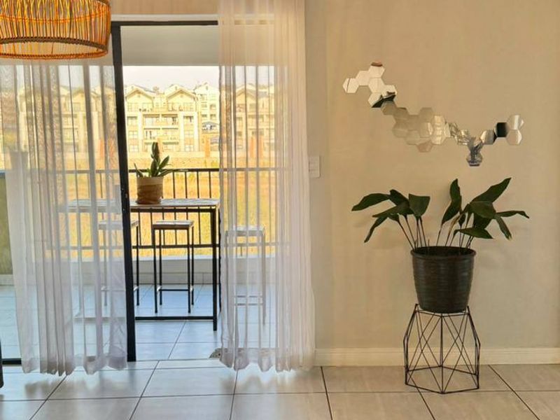 A bright living room featuring neutral tiled flooring and a large sliding glass door that provides access to an outdoor balcony area.