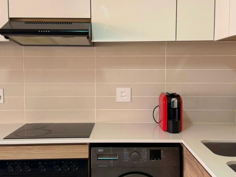 Modern kitchen featuring sleek white upper cabinetry, wood-grain lower cabinets, stone countertops, integrated appliances, and a clean tiled backsplash.